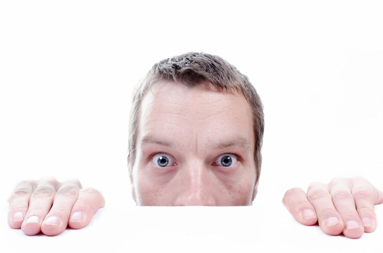 Man peeping over table top with fear or phobia