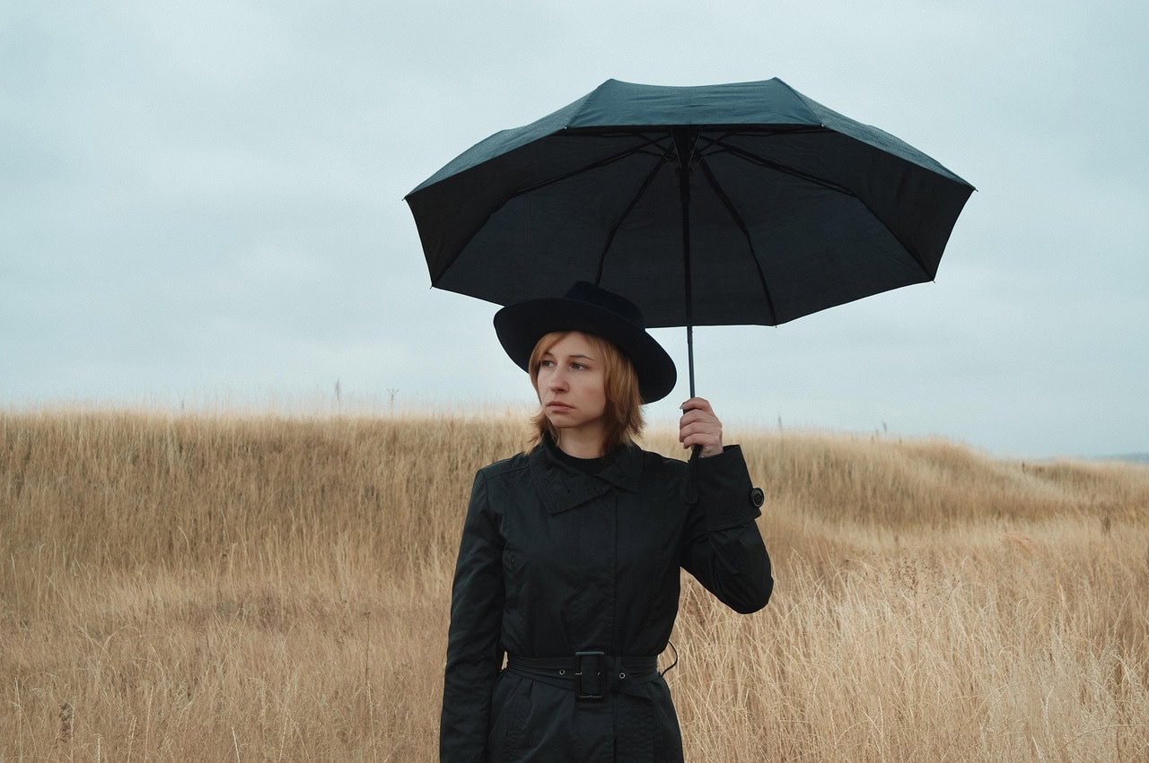 Woman in field with umbrella looking anxious or sad
