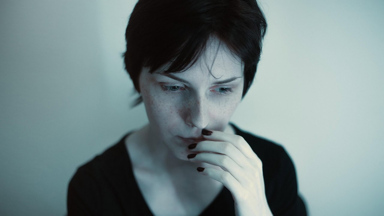 Woman looking anxious or sad, looking down. fingers to mouth