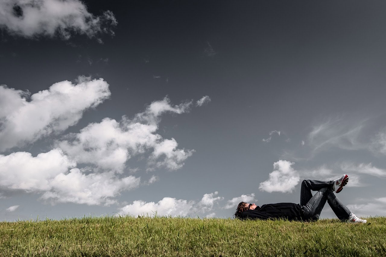 Man laying on his back on the grass clouds in sky