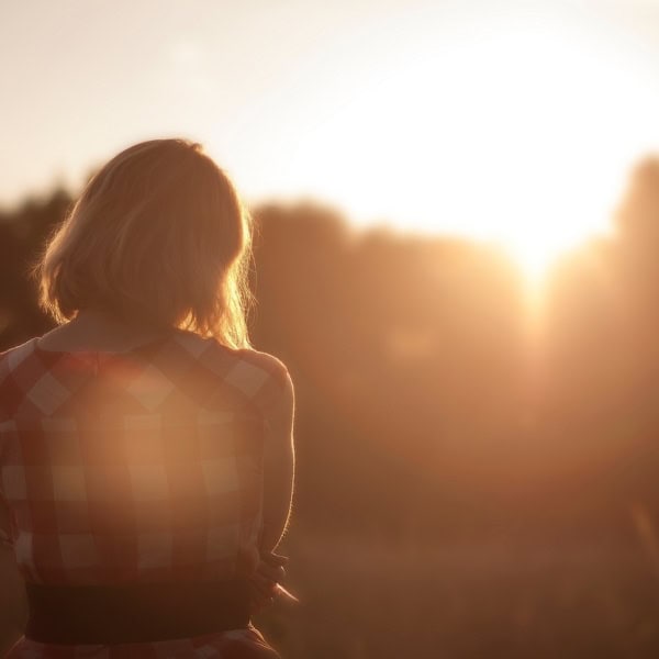 A woman from the back in a field looking towards a hazy sun