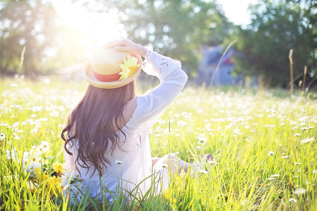 A woman from the back, sitting on grass, looking towards bright, hazy sun